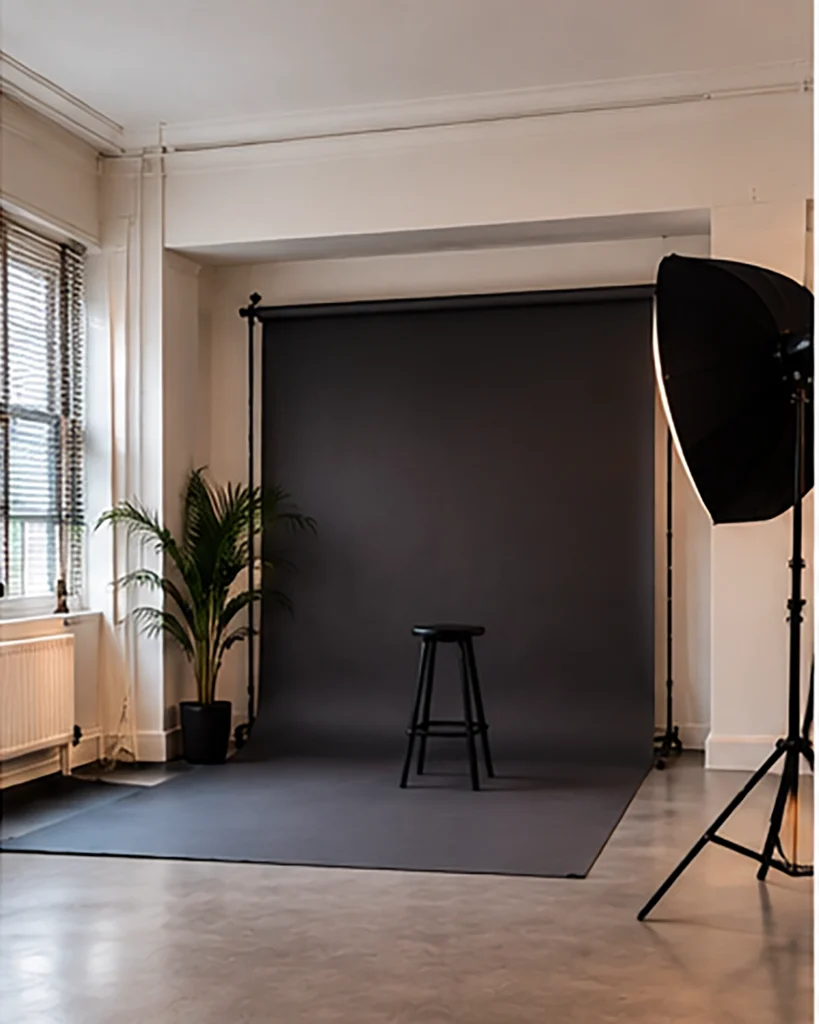 A minimalist photography studio featuring a black backdrop, a stool, and soft lighting equipment.