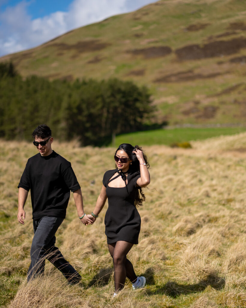 A couple walks hand-in-hand through a grassy field, enjoying a sunny day in a scenic landscape.