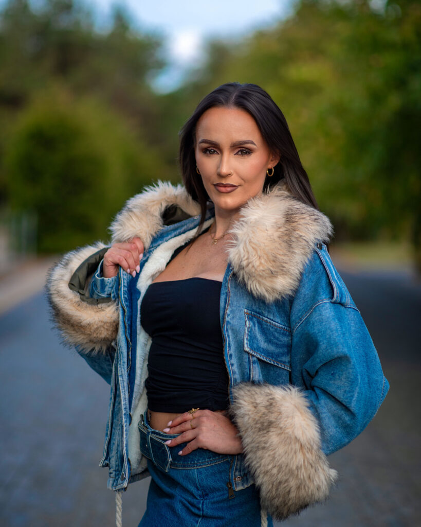Woman in a stylish denim jacket with fur trim poses confidently outdoors, showcasing a trendy fashion look.