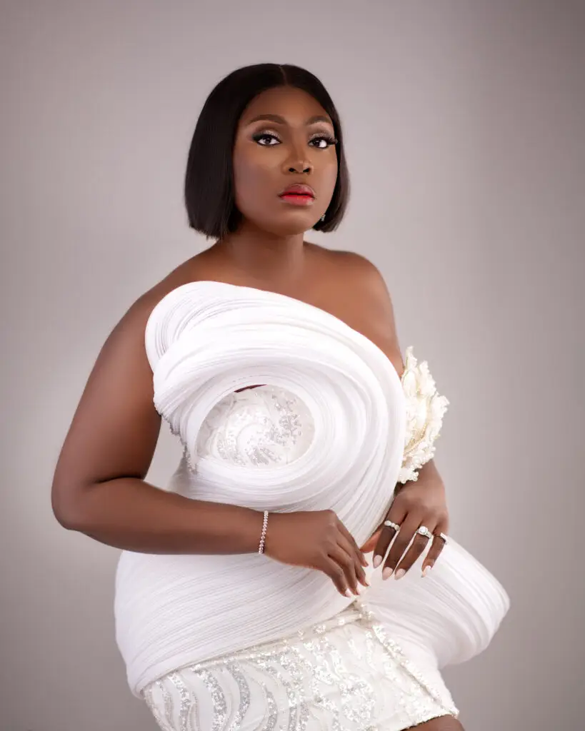 Elegant woman in a stunning white gown with intricate details and bold makeup, showcasing a unique fashion design.