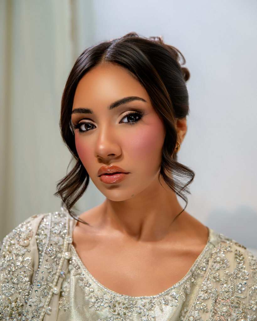 A woman with elegant makeup and a beaded outfit poses gracefully, showcasing beauty and style.
