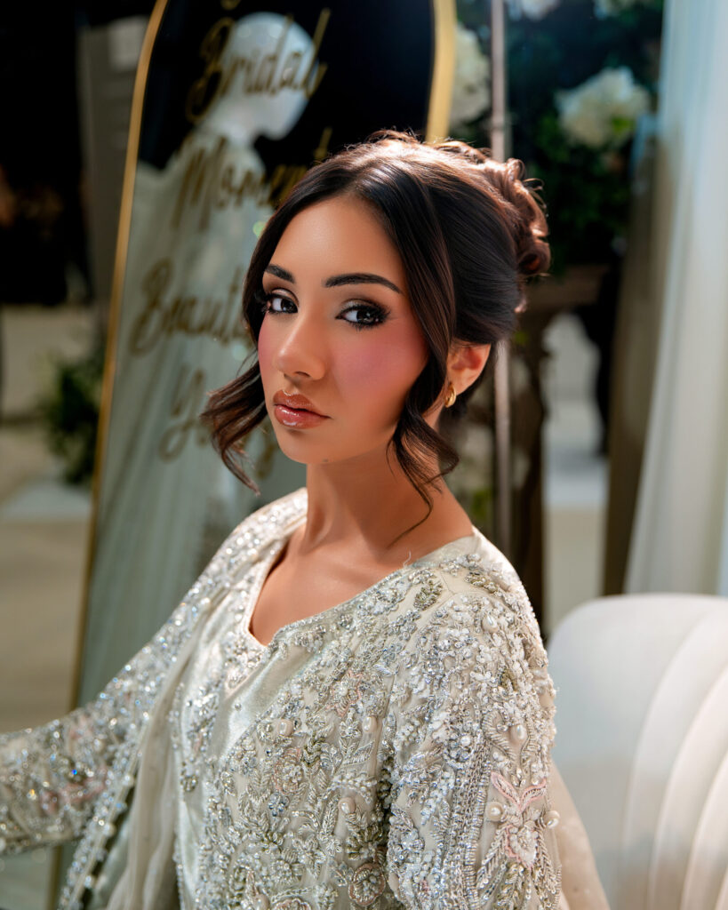 Bridal model showcasing intricate embellished attire and elegant makeup in a beautifully decorated setting.