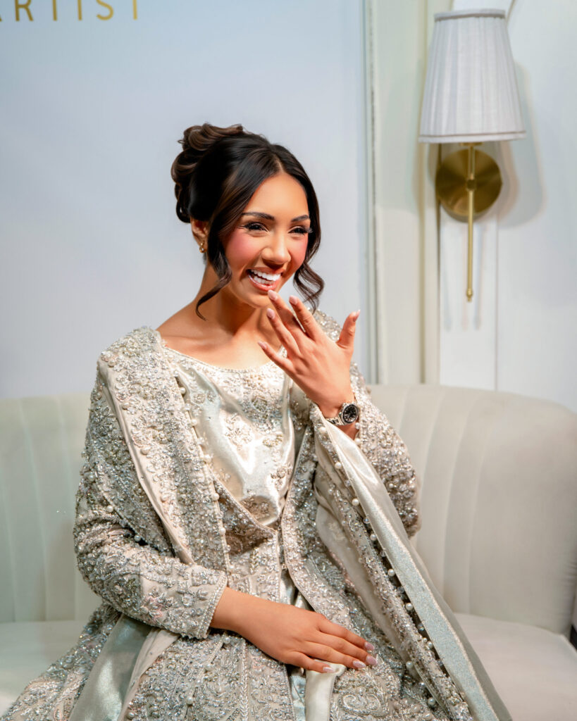 A smiling woman in an intricately beaded silver outfit poses elegantly, showcasing her style and confidence.